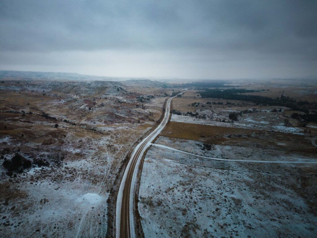 A county road in rural Dawson county Montana showing a skiff of snow snowing on bare, overgrazed spots and healthy vegetation on a small paddock that had been rested for years.